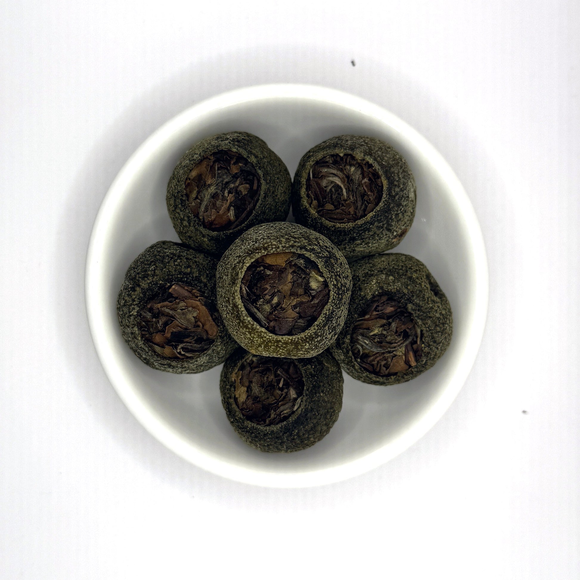 White bowl with dark green tea leaves on a white background, tangerine pu'er