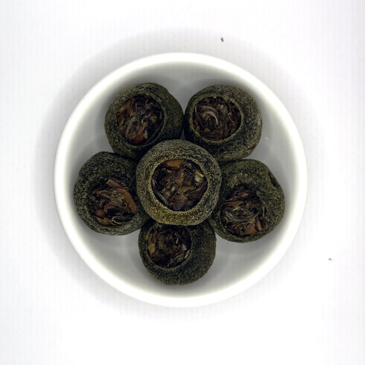 White bowl with dark green tea leaves on a white background, tangerine pu'er
